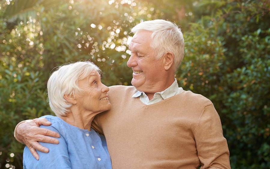 A smiling mature man and woman in their yard represent the improved quality of life with ALS treatment.