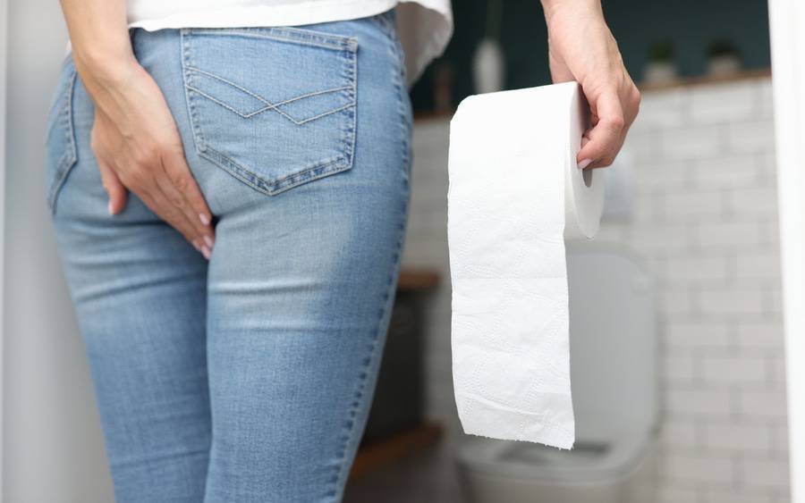 Woman grabs butt while holding soft toilet paper.