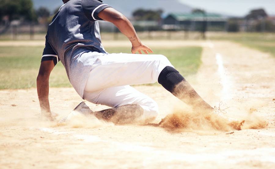 Baseball player sliding into home base, illustrating how athletes may need a sports medicine physician.