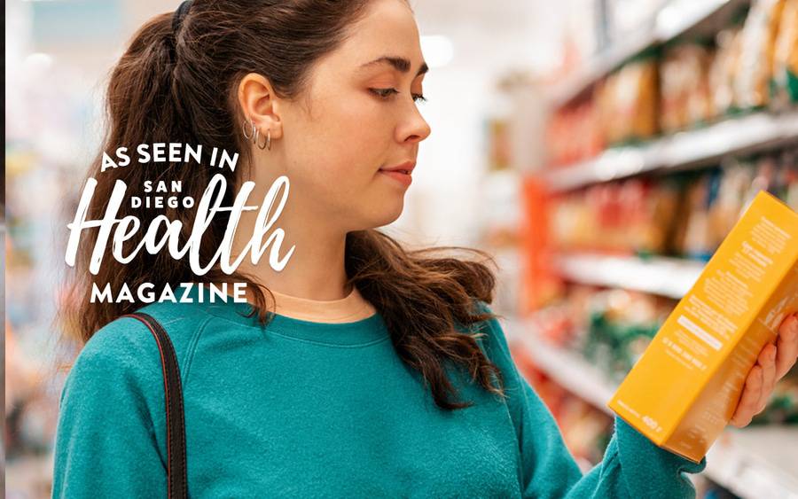 A woman stops to read a label on a food product while shopping in a grocery store. - San Diego Health Magazine