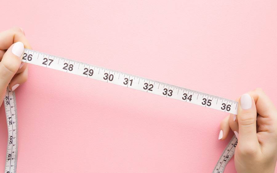 A waist measuring tape helps illustrate an article on how to safely lose belly fat over time.