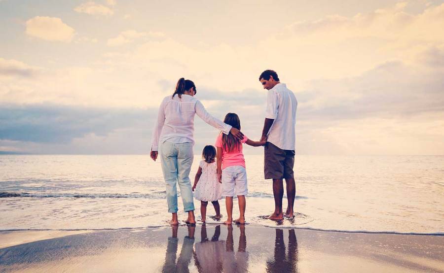 Man, woman and two small children stand on the ocean shoreline on a cloudy day.