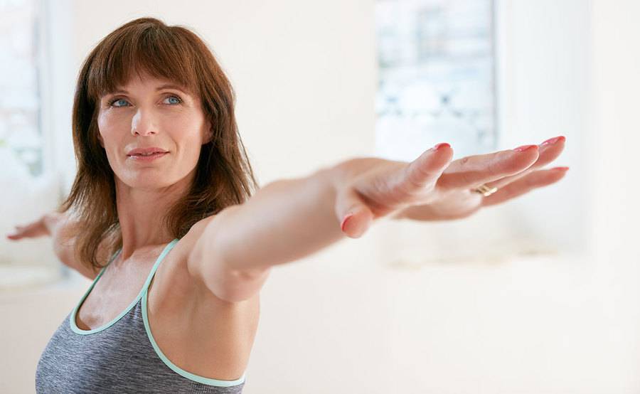 A peaceful middle-aged woman practices a yoga pose in a sports bra, representing the confidence gained from breast augmentation.