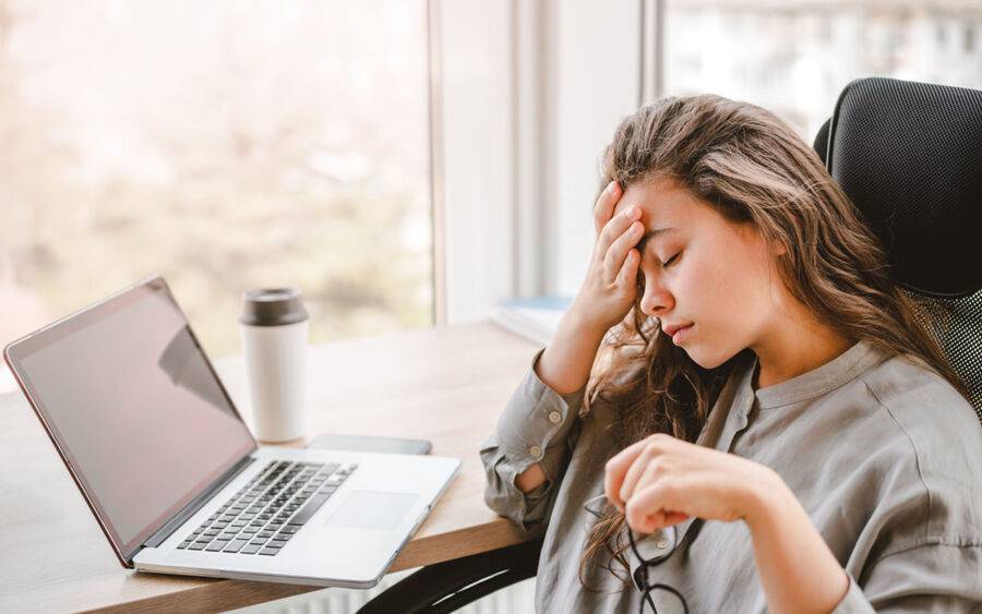 A young woman looks tired in front of her laptop, a sign of job burnout.