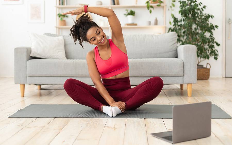 An African-American woman exercises while watching a TV program on her laptop.