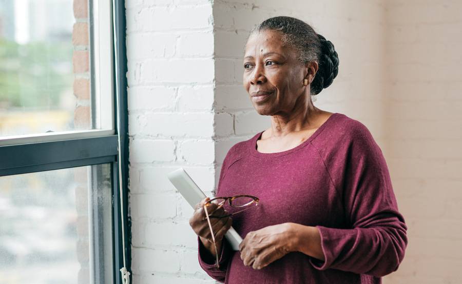 A mature African American woman stands by a window and is concerned about her multiple myeloma diagnosis.