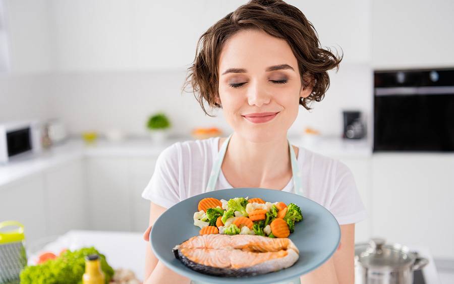 A young woman closes her eyes and smells the healthy meal she prepared.