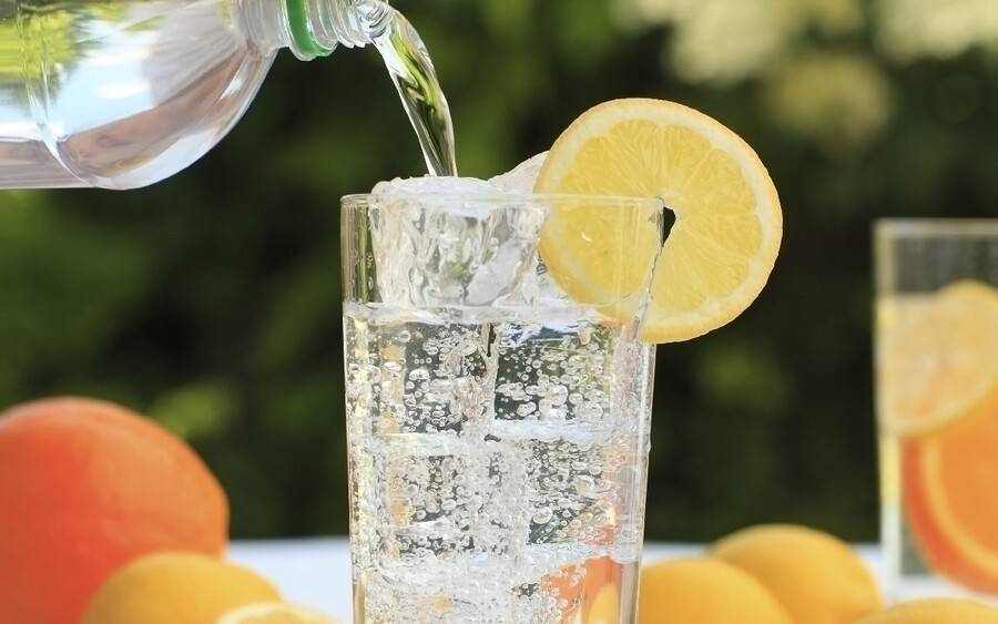 A carbonated, bubbly drink is poured into a glass with lemon wedge.