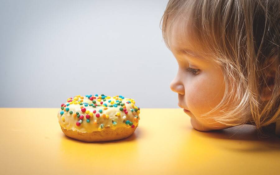 A little girl stares at a not-so-nutritious but sweet doughnut.