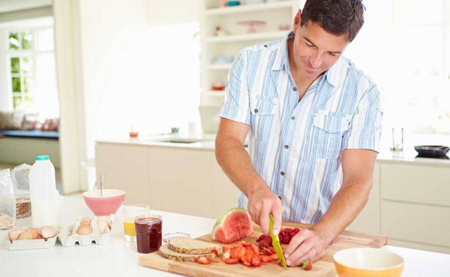 A healthy man slices berries for a low-cholesterol meal in his kitchen.
