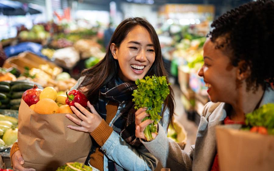 Two women smile to each other while shopping for healthy fruit and vegetables.