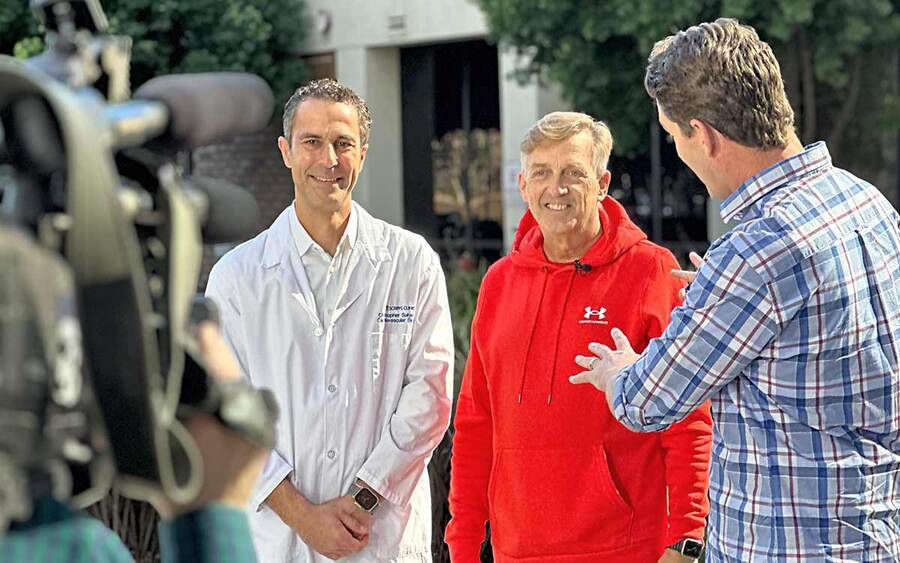 Heart attack survivor and comedian, Mark Whitney, wears a red sweatshirt and prepares to tell his heart story to local media.
