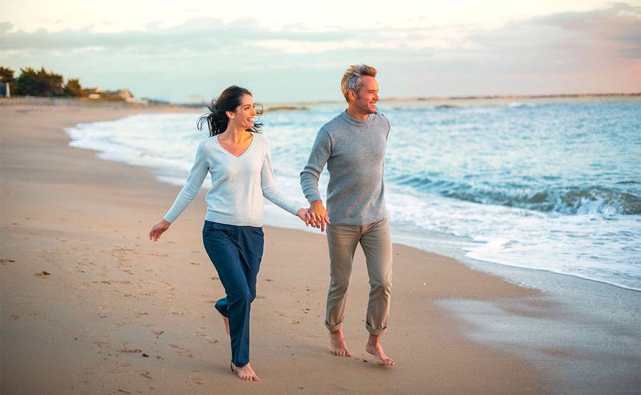 Two smiling middle-aged adults hold hands while walking on the beach, representing Scripps Executive Health services in San Diego..