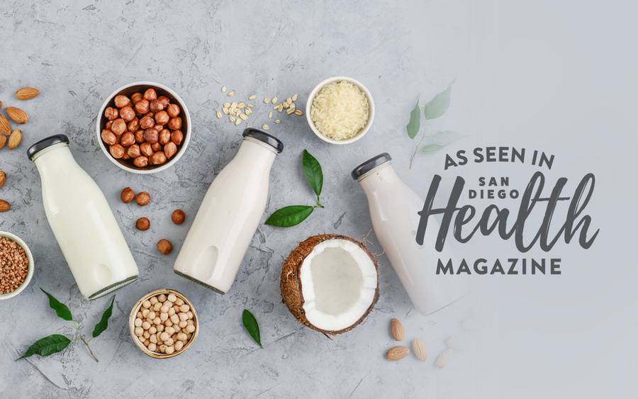Three bottles of plant-based milk lay on their sides next to nuts and an open coconut.