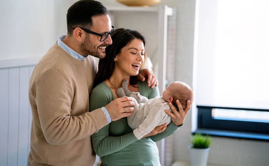 A mother and father holding their newborn baby at home while smiling.