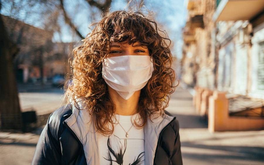 A young woman wears a face mask on a city street, representing the public service campaign #MaskUp. 