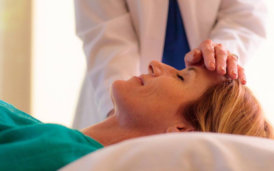A provider touches the forehead of a patients head who is lying on an exam table.