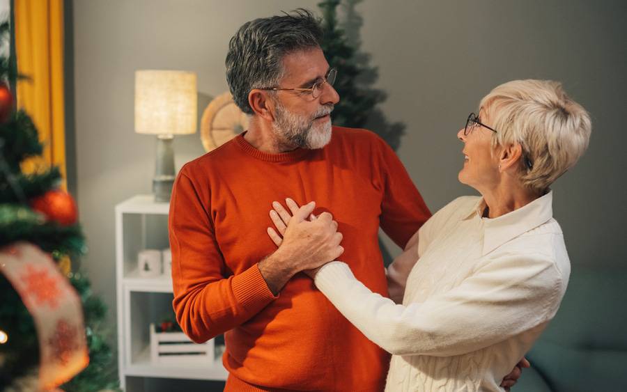 A woman places her hand on on her husband's chest at a holiday celebration with Christmas trees in the background.