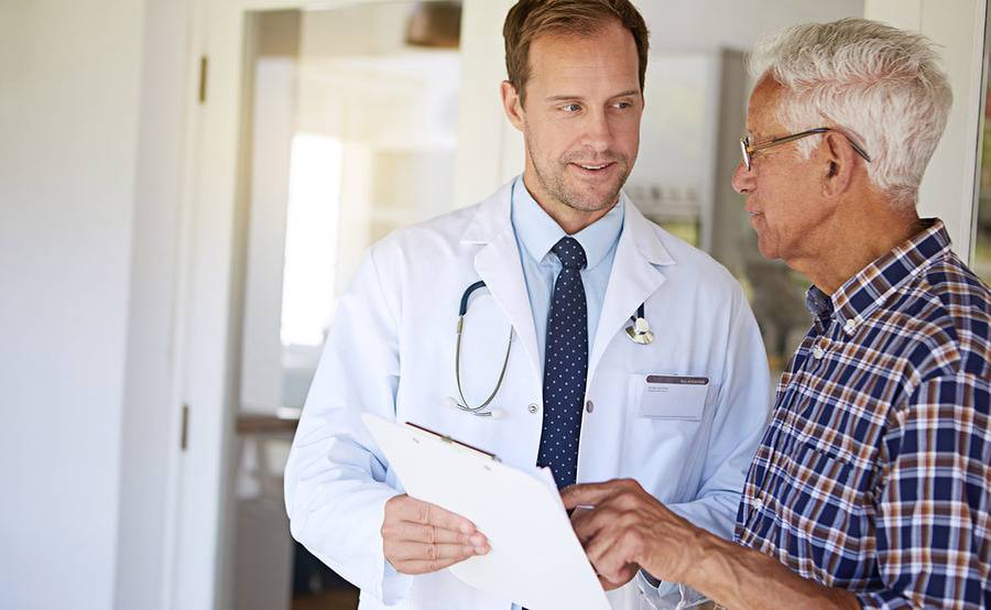 A male doctor speaking with an older male patient about cancer therapy options, including immunotherapy.