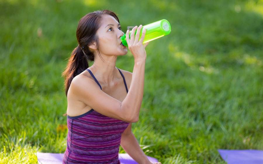 A woman drinking water while on a break from exercising.