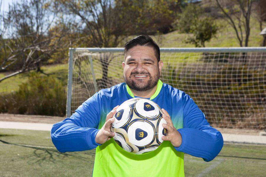 Juan Ramos smiling holding a soccer ball in front of a goal.