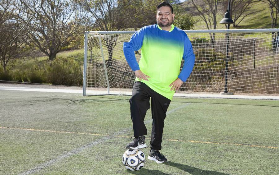 Juan Ramos, a kidney transplant patient, is standing in front of a goal with a soccer ball.