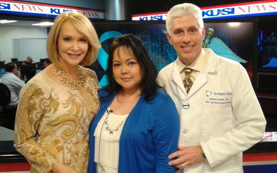A young woman in a blue sweater who is a Scripps colorectal cancer patient stands with a KUSI news anchor and Scripps doctor.