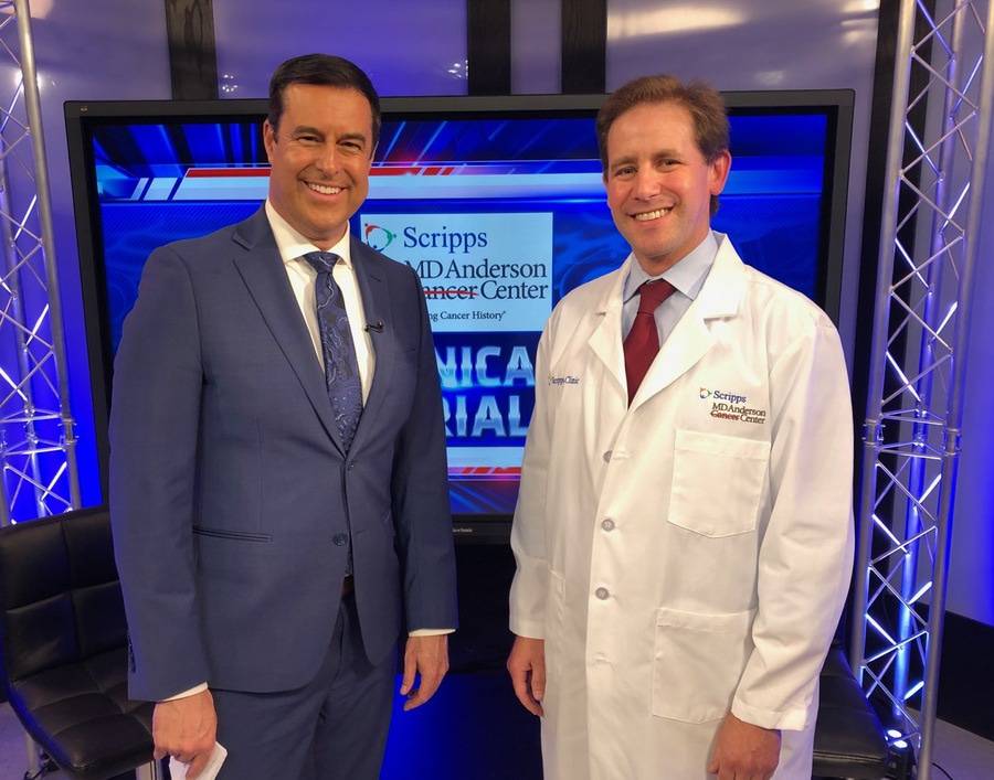 A San Diego news anchor and Scripps oncologist smile for a photo during a news segment recording.