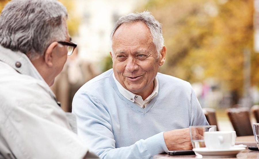 A smiling mature man having coffee with a friend represents the importance of lung cancer screening and prevention.