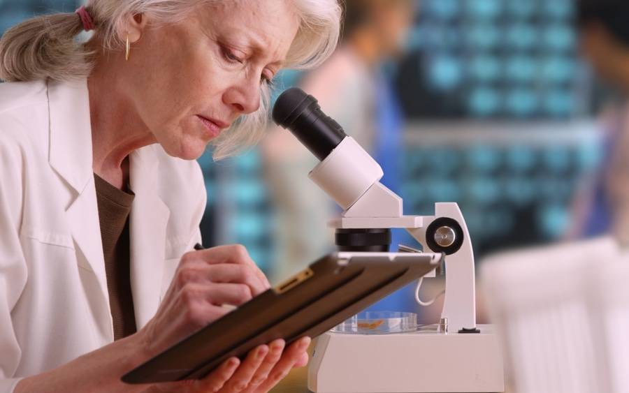 An older clinical employee takes notes while doing work in laboratory.