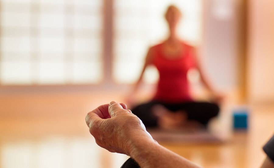 A close-up of a person's hand resting on their knee during a meditation classes,