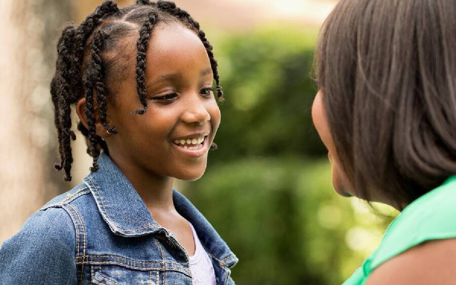 A smiling young girl has a conversation with her mother in an outdoor garden environment