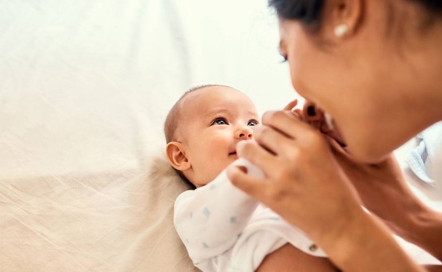 A mother smiling at her baby while the baby lies on its back, smiling back at her.