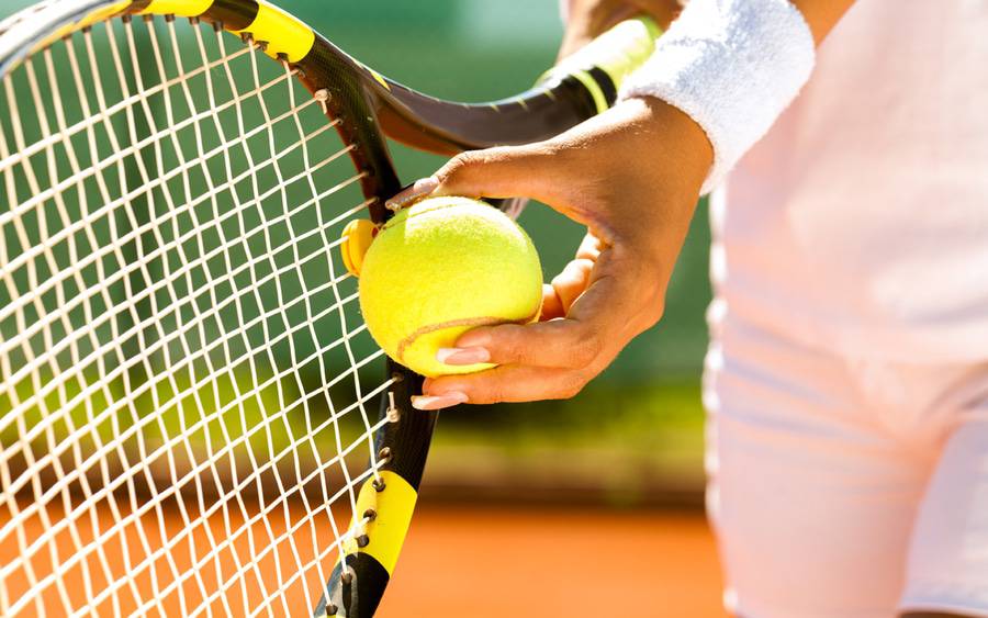 A woman's hand prepares to serve a tennis ball with a racket representing a Scripps cancer doctor's recent tennis win.