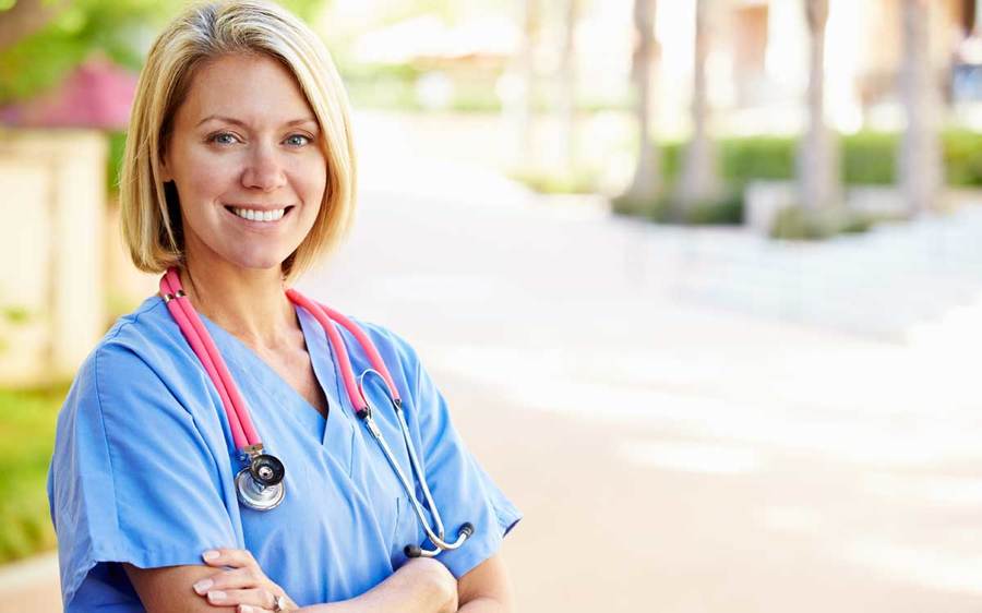 A nurse in blue scrubs stands outside, representing the best health care workplaces in the US.