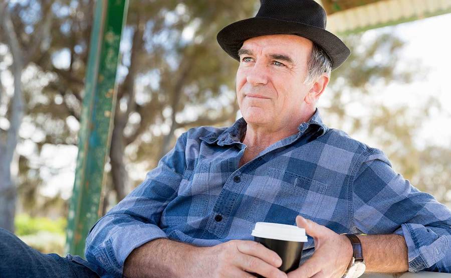 A smiling middle-aged man drinking coffee in a park represents the full life that can be led after parathyroid cancer treatment.