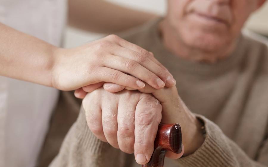 Caregiver holds hand of elderly man with Parkinson's disease.