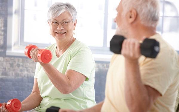 An older man and woman participate in a strength training class using light, hand weights.