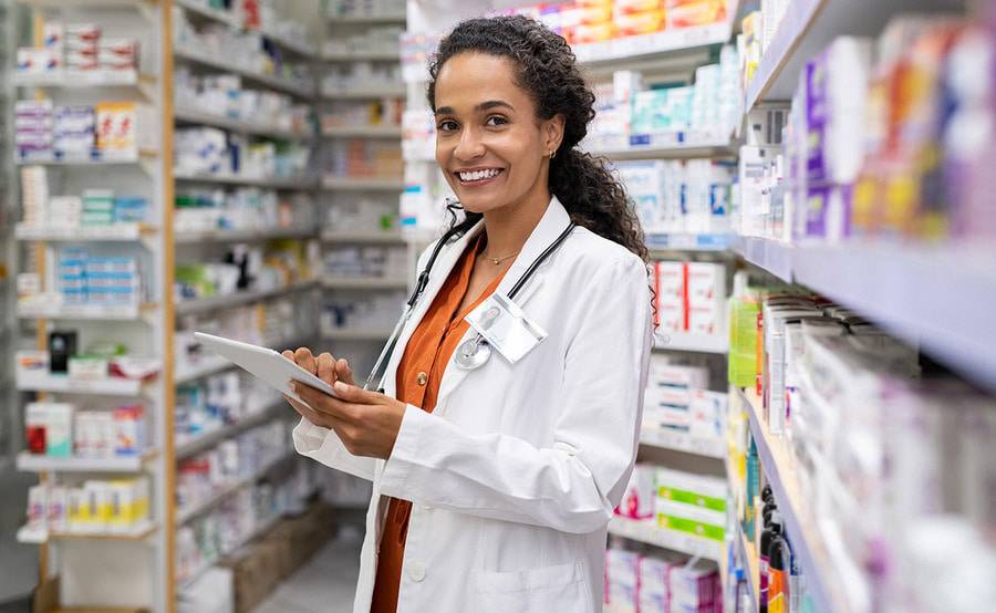 A young female pharmacist smiles as she checks her tablet in the pharmacy.