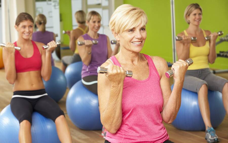 An older woman works out with other women, trying to reduce weight gain after menopause.