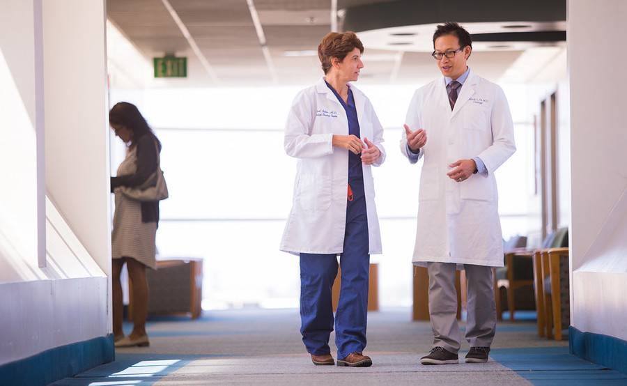 Two doctors talk while walking in a sunny corridor, representing collaborative robotic urologic surgery at Scripps.