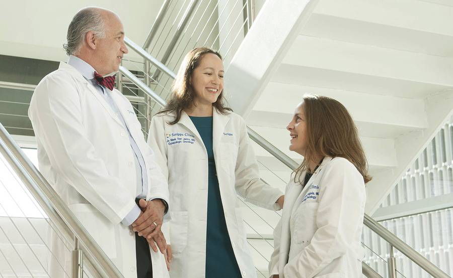 A male doctor and two female doctors gather on a staircase in a clinic setting to discuss aspects of gynecologic cancer.