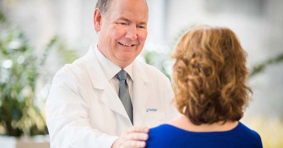 A mature male cancer doctor reassures female patient, representing Scripps expert offering insights on cancer trends.