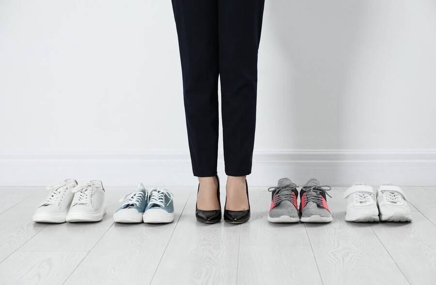 A woman stands next to a row of shoes to try on, looking for one that is comfortable and will not cause any foot pain.