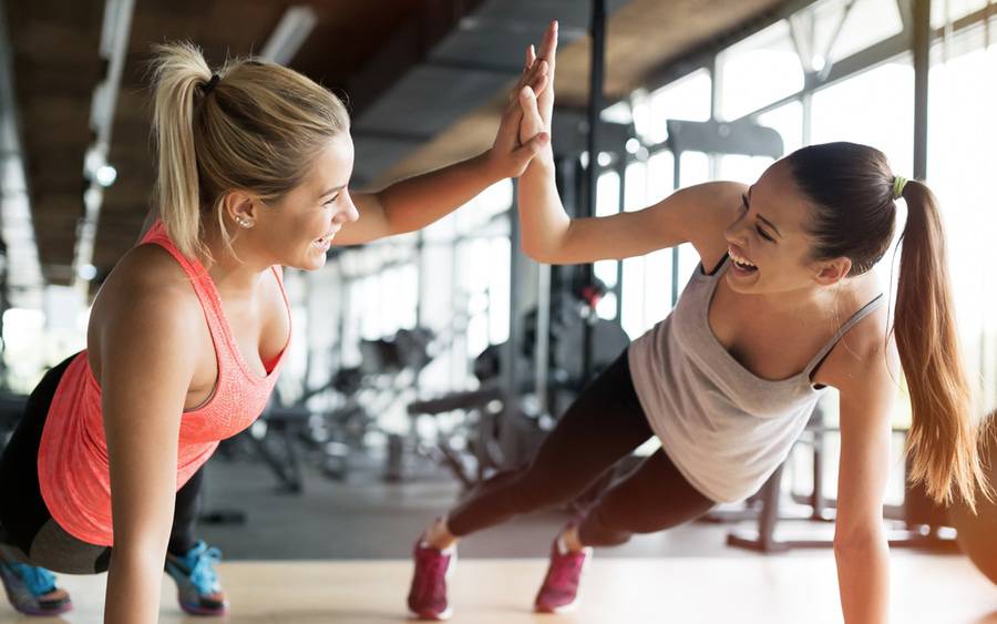Two young women have fun while stretching and working out together.