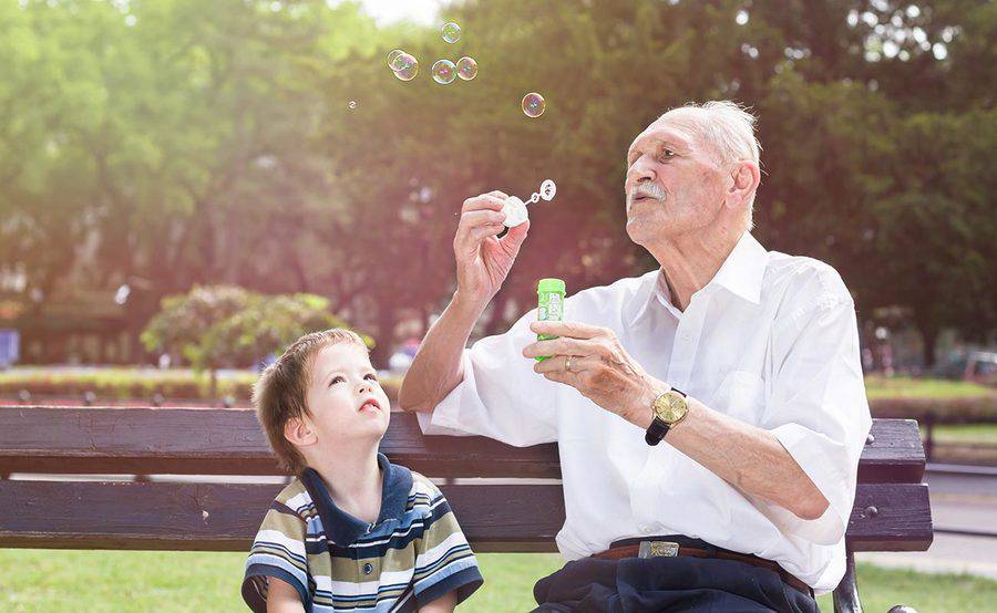 A mature man blows bubbles with his grandson on a park bench, representing the importance of stroke prevention.