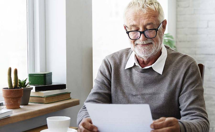 A smiling mature man reads paperwork over a cup of coffee, representing the improved quality of life that can be gained from quick treatment for stroke.