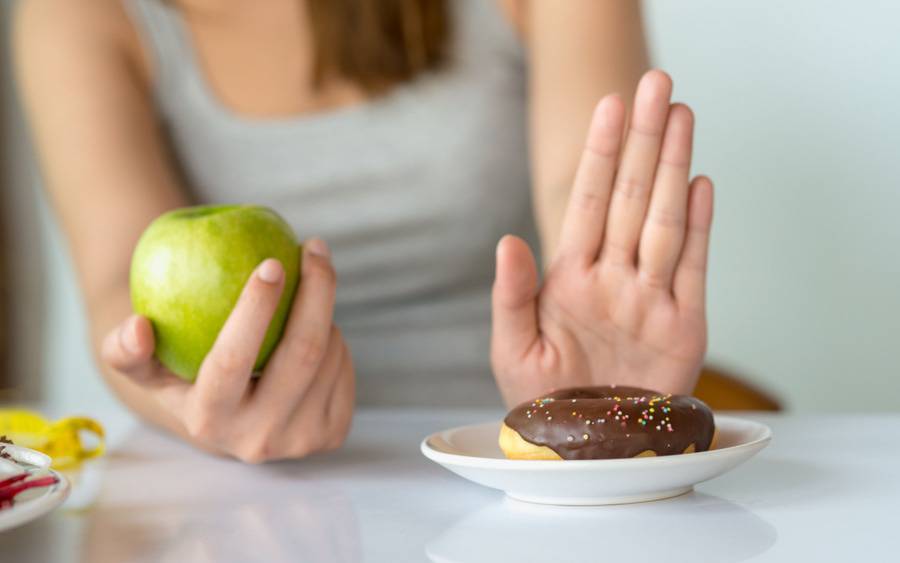 Woman using one hand  to resist eating a doughnut while holding a healthy apple that she plans to eat.