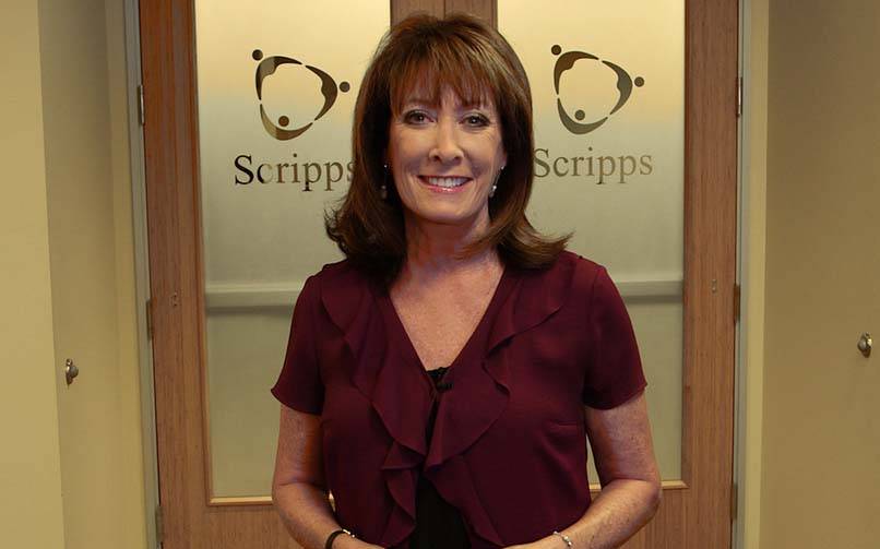 A smiling Susan Taylor portrait standing before two doors embossed with Scripps logo.