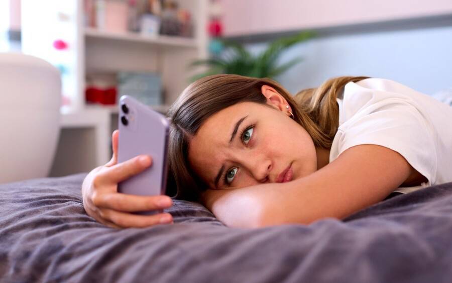 A teen girl stares at her phone, feeling depressed.